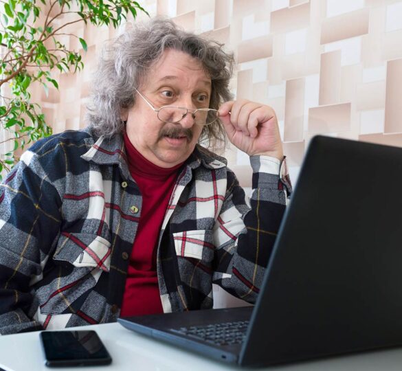 an older man removes his glasses while looking at laptop computer